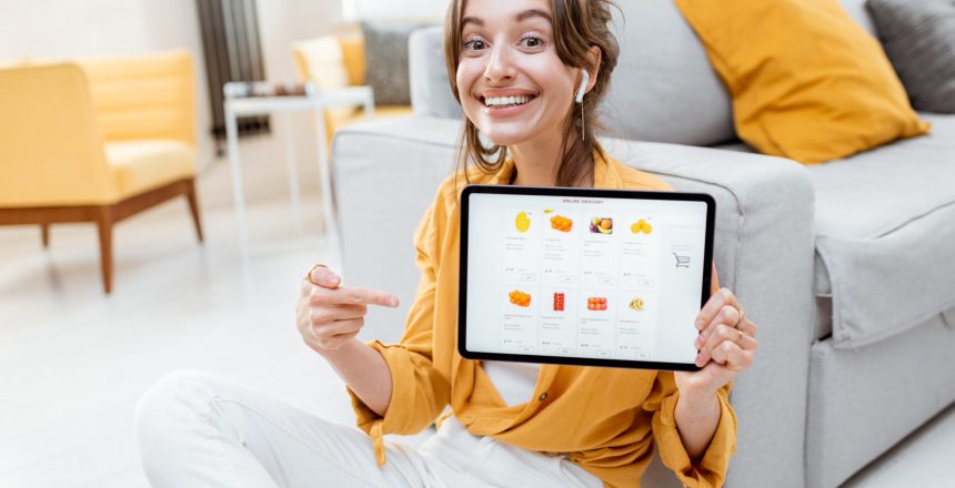 Young and cheerful woman showing a digital tablet screen with launched online store, shopping online at home. Concept of buying online using mobile devices